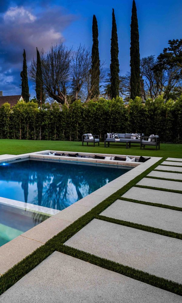 Modern luxury house exterior with a swimming pool, lounge chairs, and outdoor seating area at dusk.